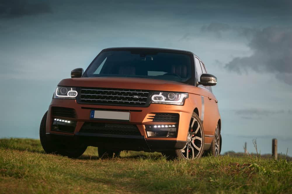 This is an orange Land Rover Range Rover on a grass field.