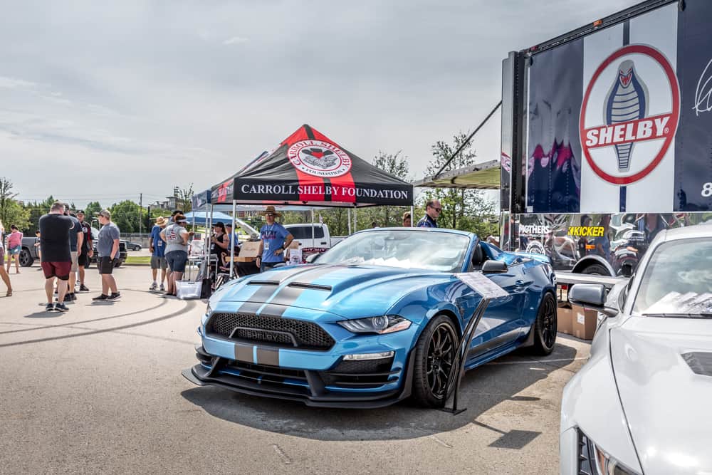 Front view of a sky-blue Ford Mustang GT parked with people behind.