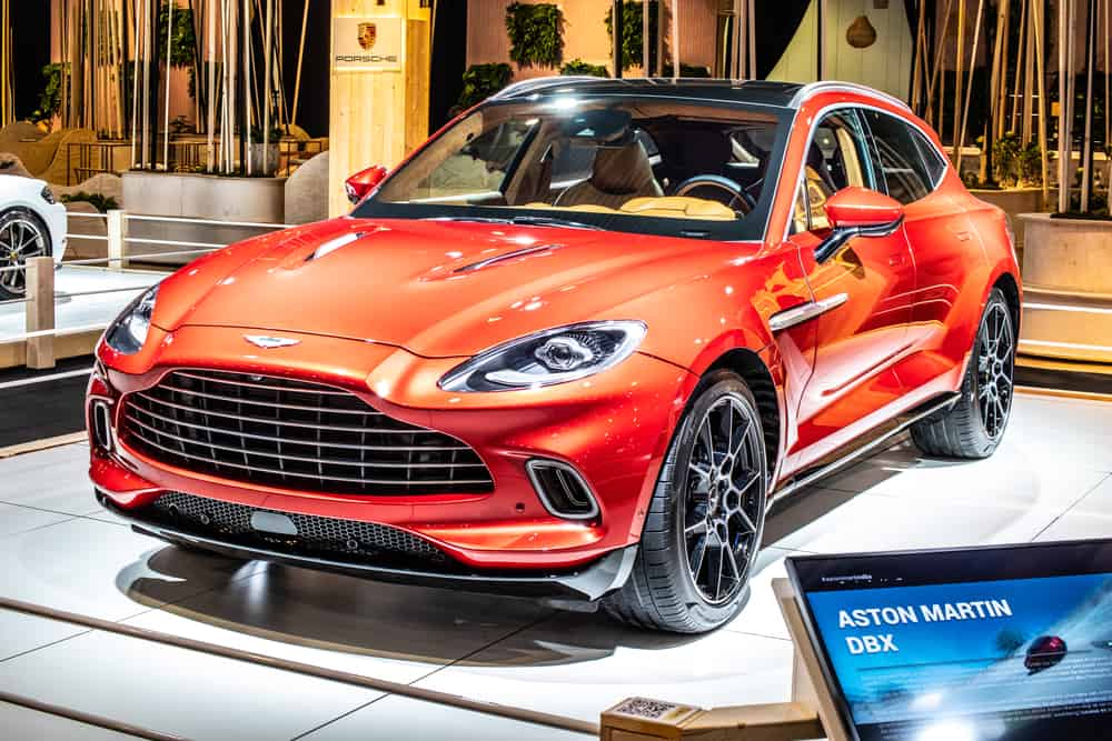 A photo of Aston Martin DBX ain orange color at the auto show.