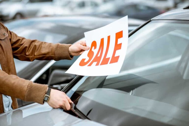 This is a car salesman putting a sale sign on a used car.