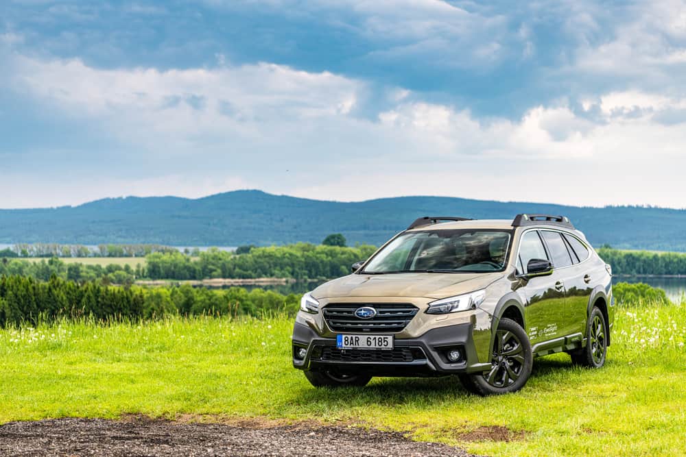 Subaru Outback parked on the field with mountain background.