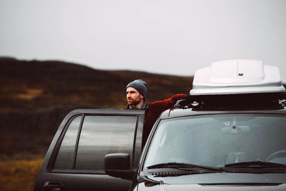 A man standing in front of the car open door in mountain hill area.