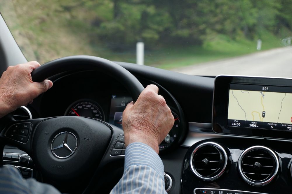 An old man's hand holding the car steering wheel.