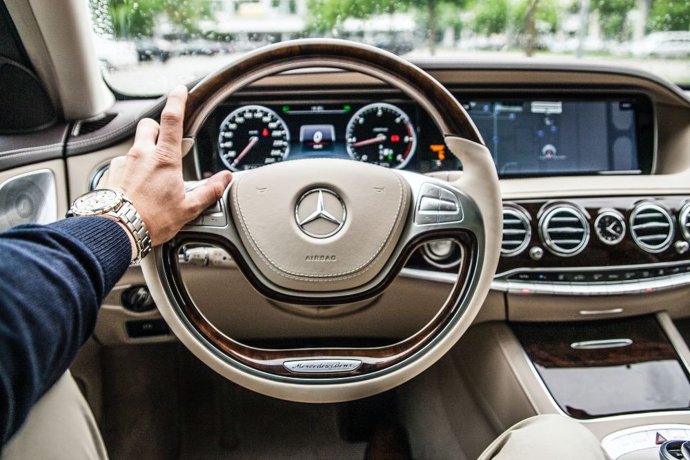 A man's hand grips the steering wheel of a car.