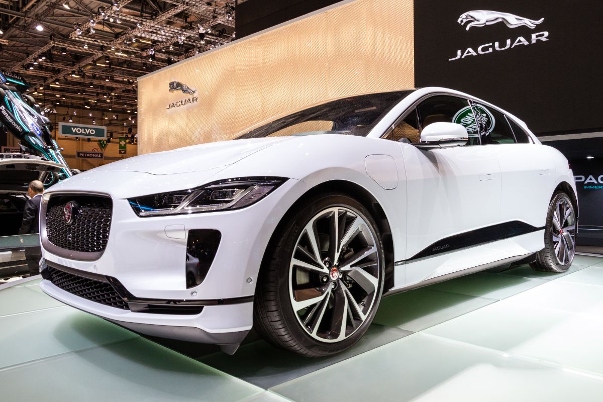 A white Jaguar I-Pace car with a Jaguar logo at the wall.