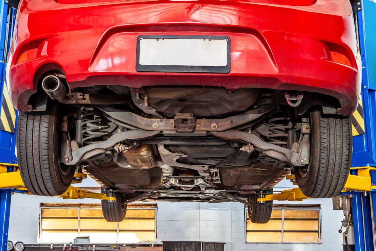 The undercarriage of hanging red car in auto shop.