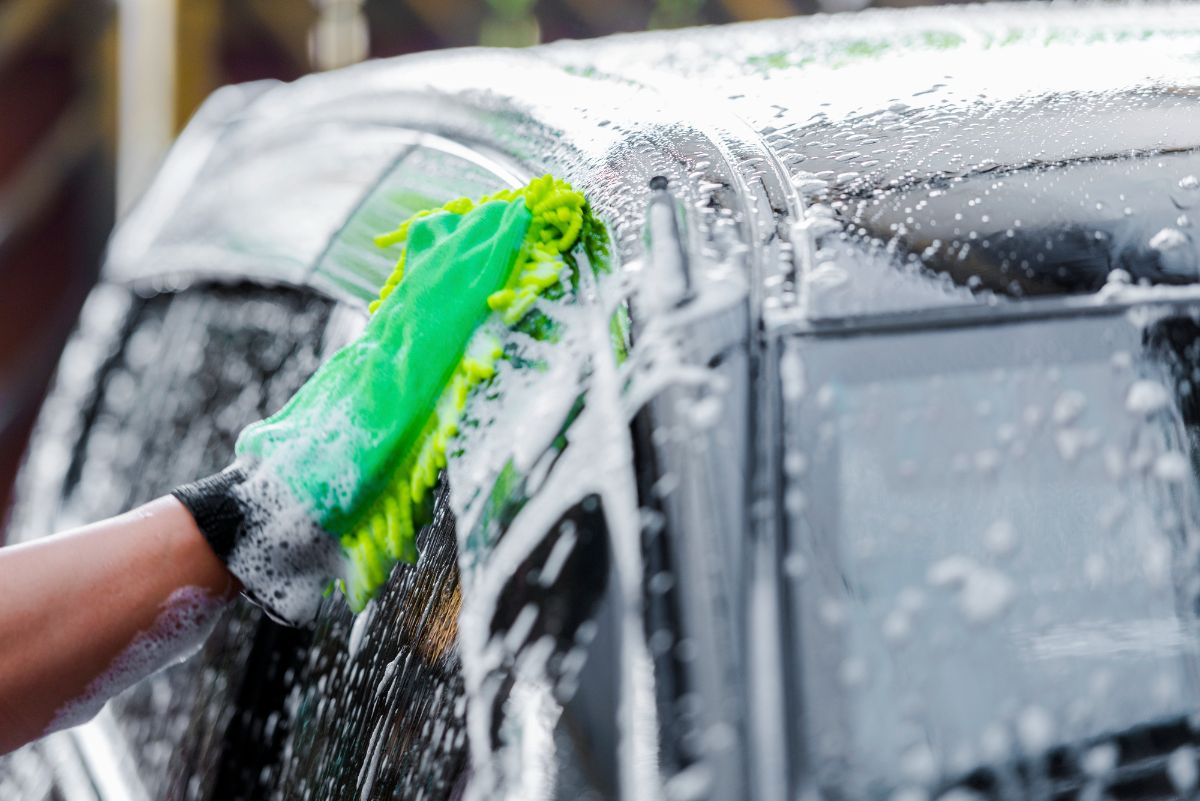 Hand washing the black car using soap and cloth sponge.