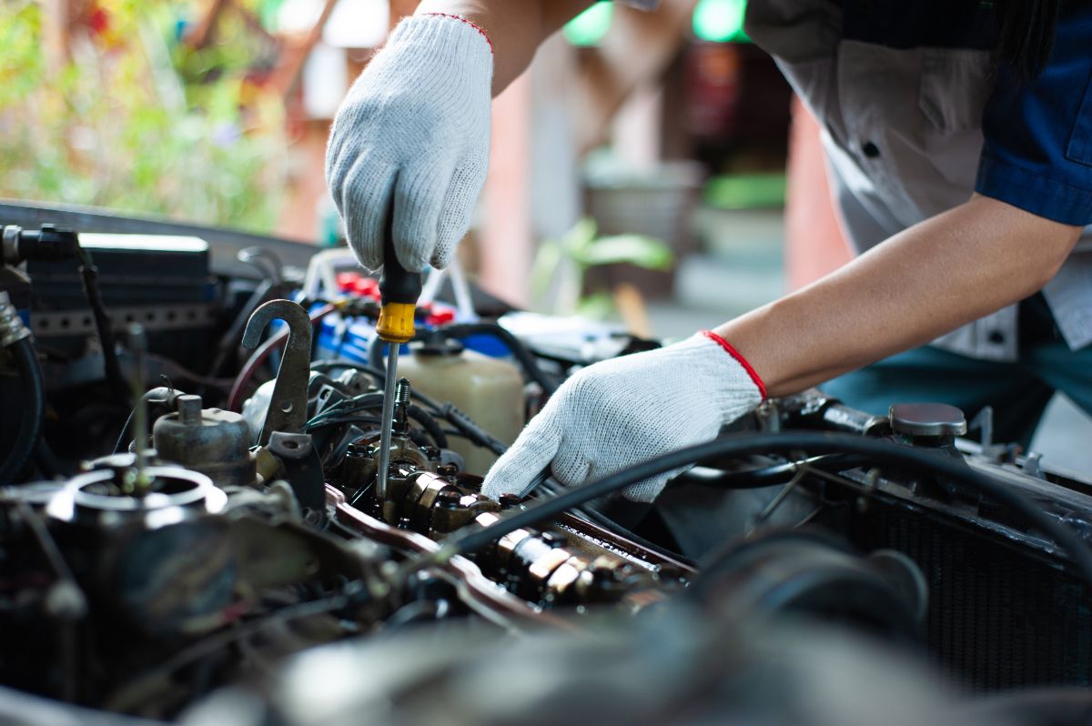 Close up photo of a mechanic repairing something in a car;s engine.