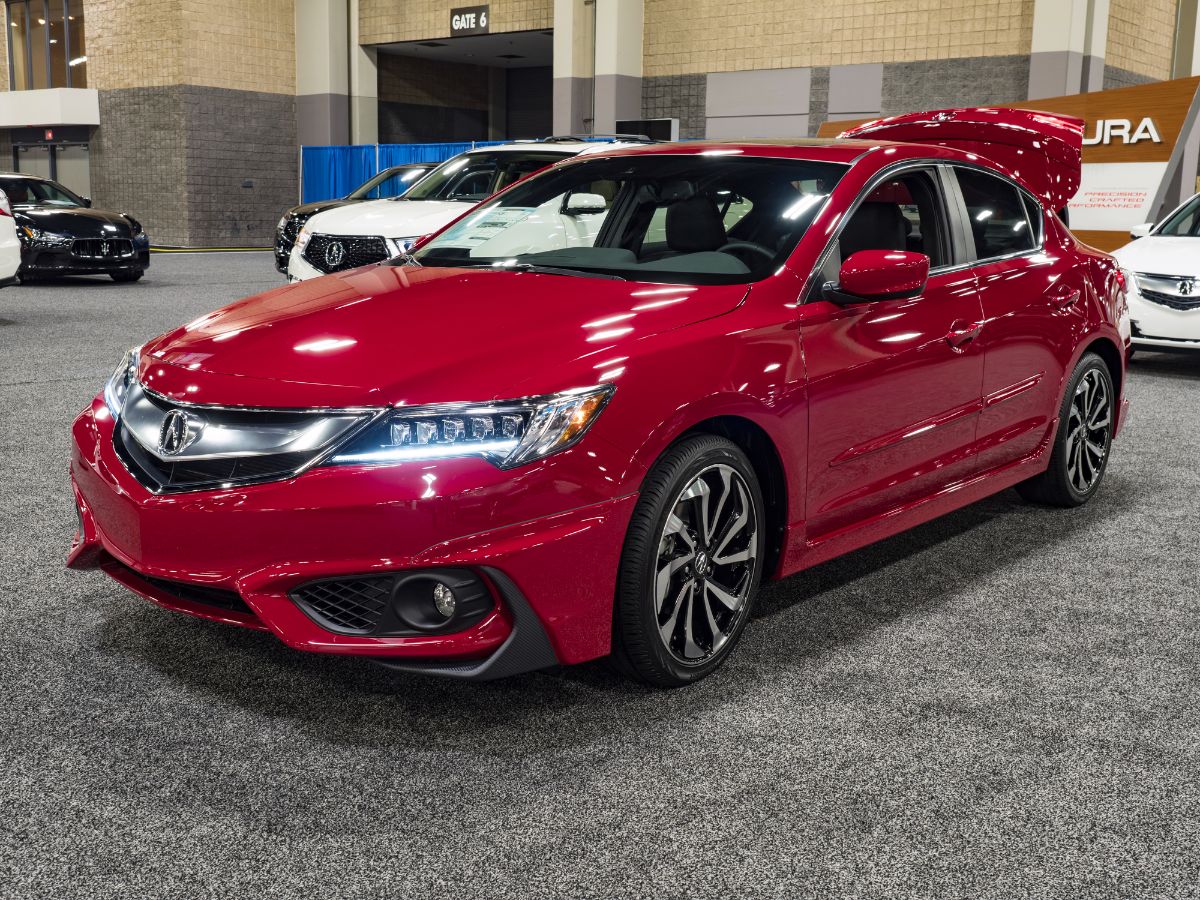 A front shot of a glossy red Acura ILX on display with front lights on.