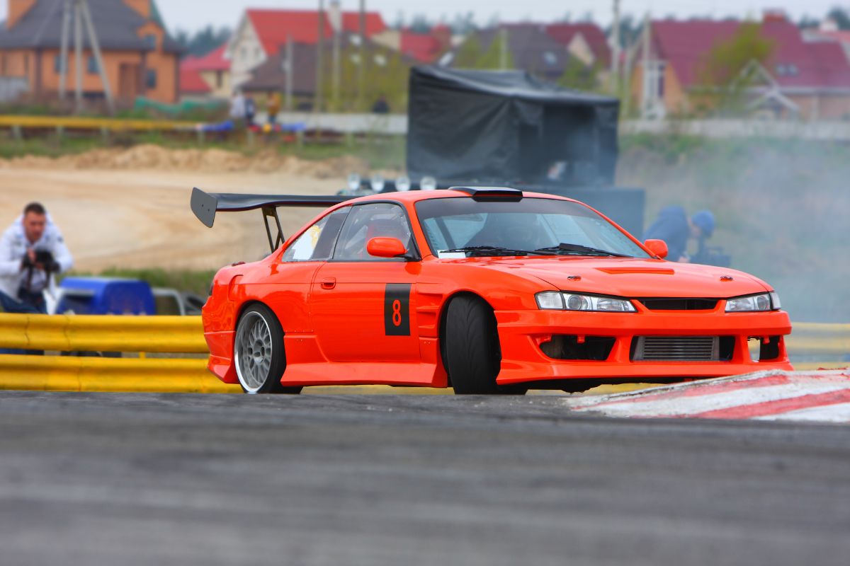 Red racing car drifting on road with carbon fibers spoiler.