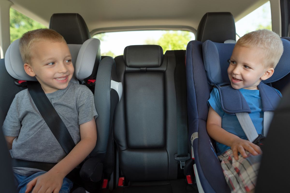 Two little boys are buckled in booster car seat.