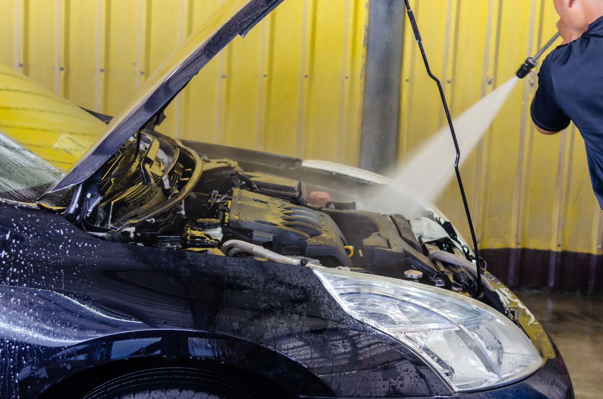 Man washing the car engine with high pressure water.