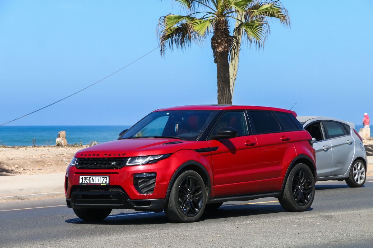 Side view of red Range Rover Evoque on road near the sea.