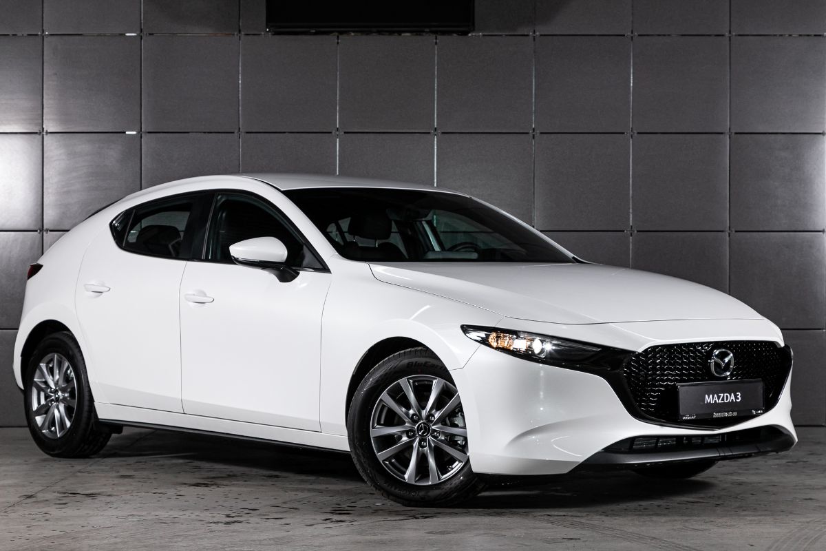 Right side view of a white Mazda Mazda3 parked on a gray tiles background.