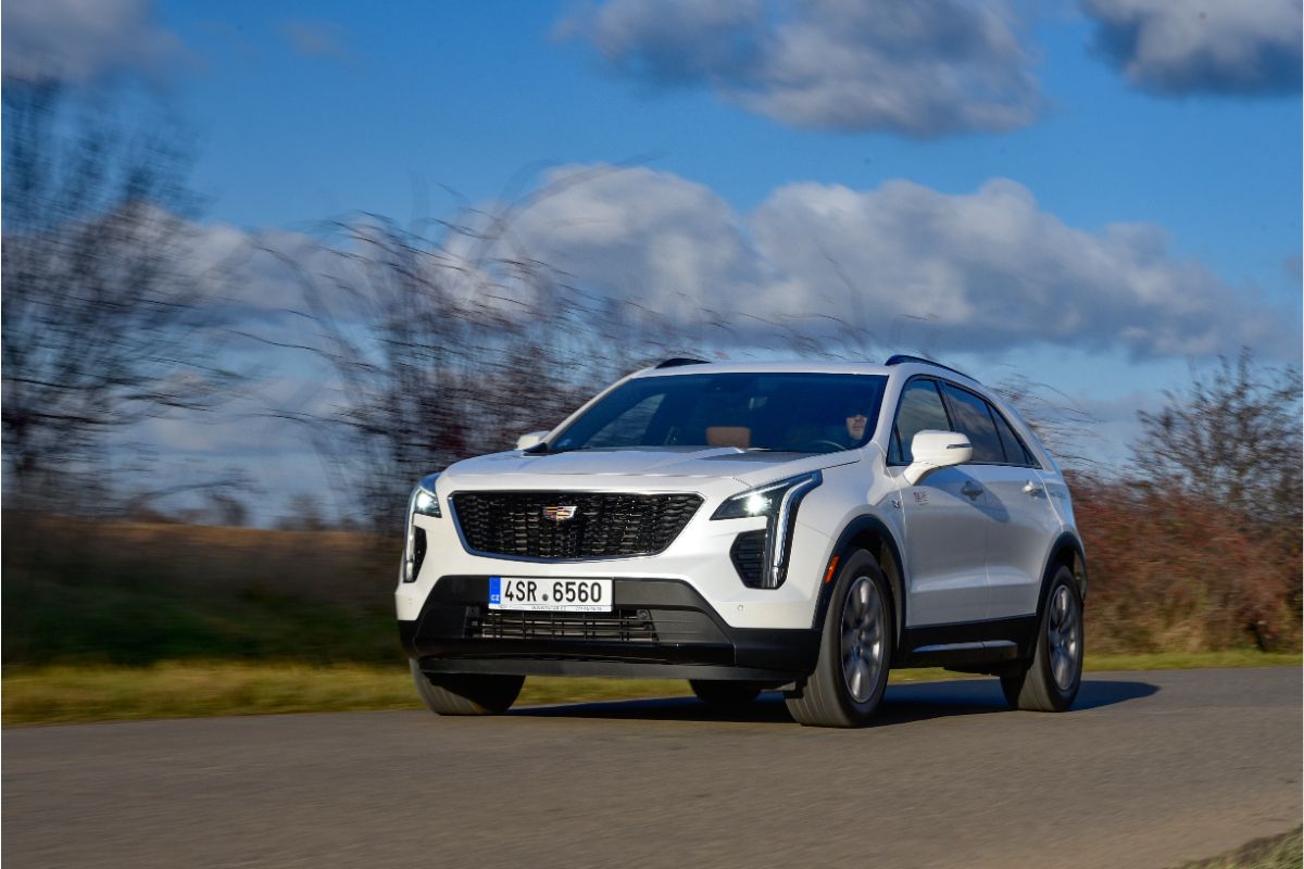 A white cadillac xt4 in the middle of road moving.