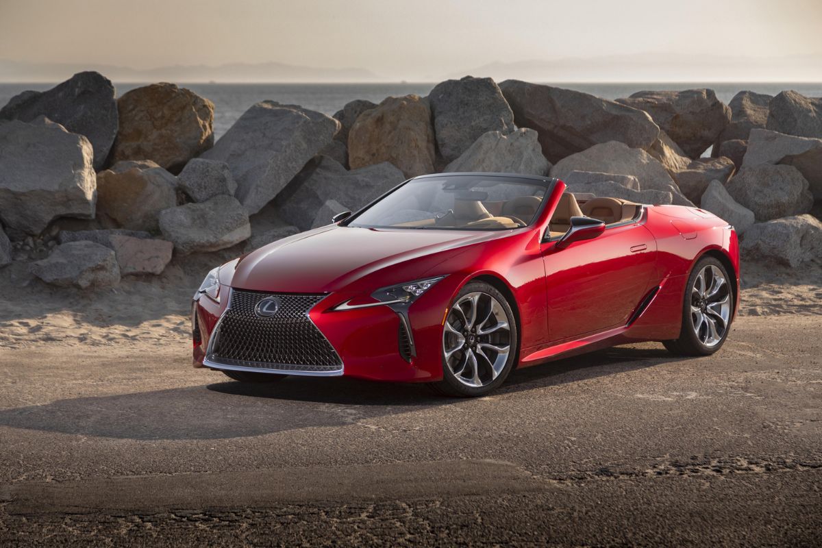 The all new Lexus LC500 in red colorway spotted parking at a seaside with big piled rocks in the background.