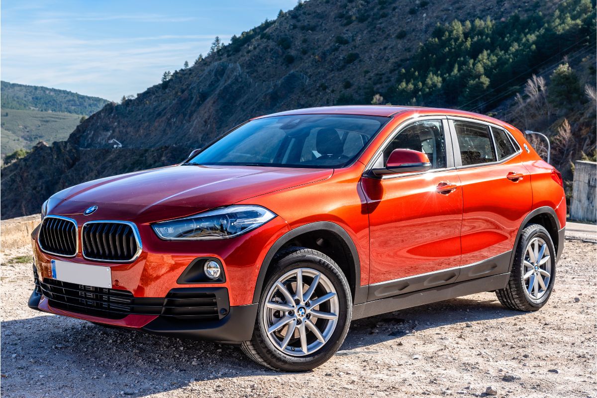 Side view photo of red bmw x2 parked on dirt road in mountains.