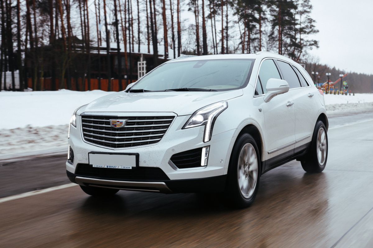 A photo of cadillac xt5 car in a white color driving in the street during winter.