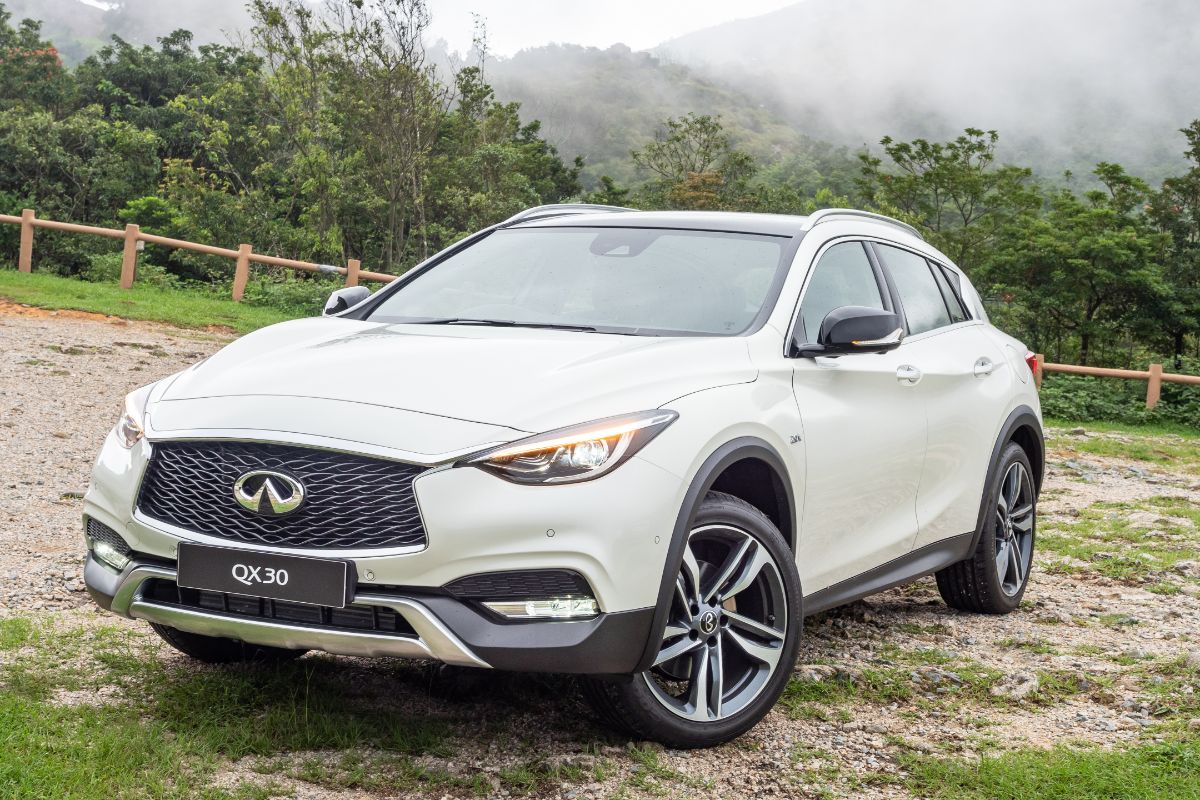 Cose up photo of white infiniti qx30 car test driving on mountain raod.