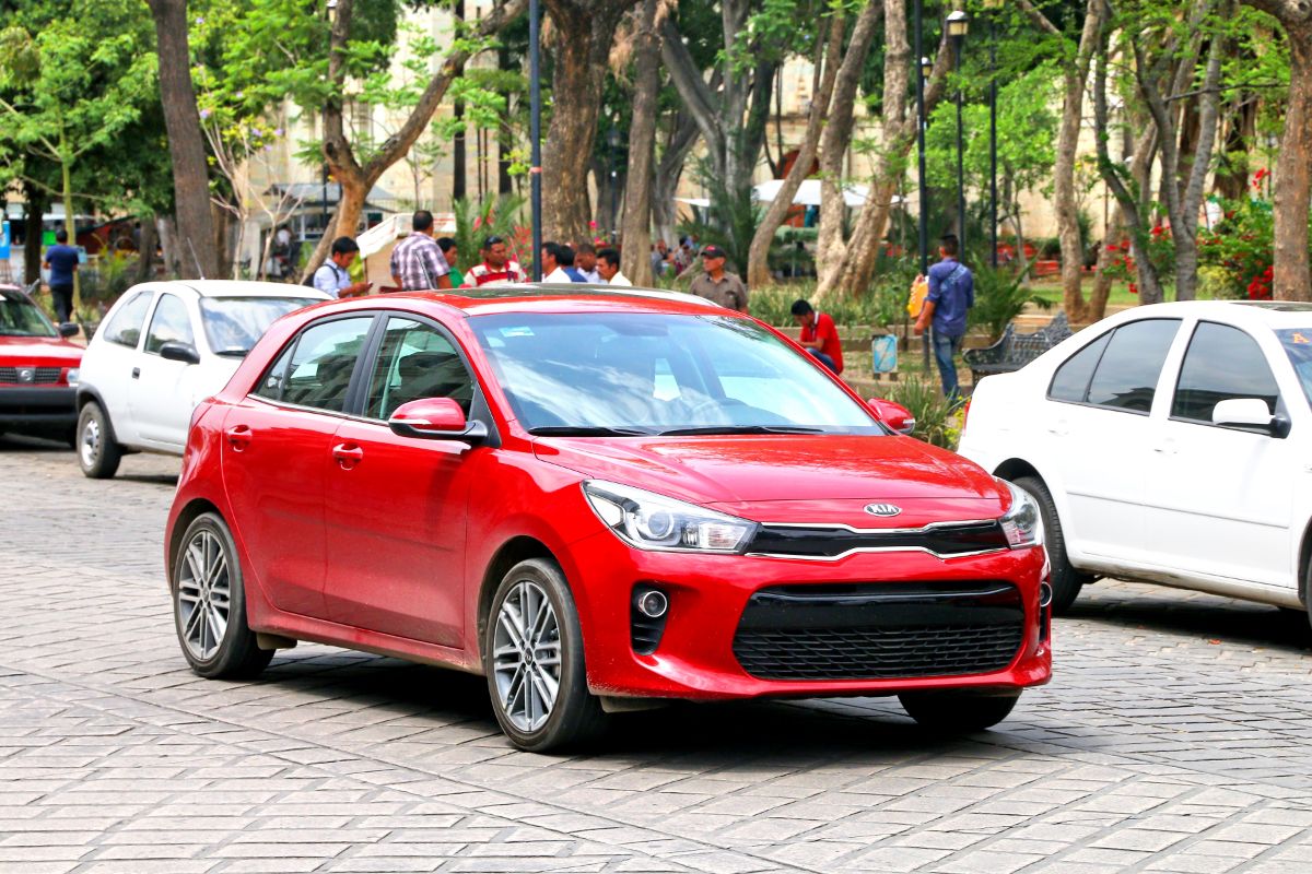 A red kia rio hatchback driving in the city street.