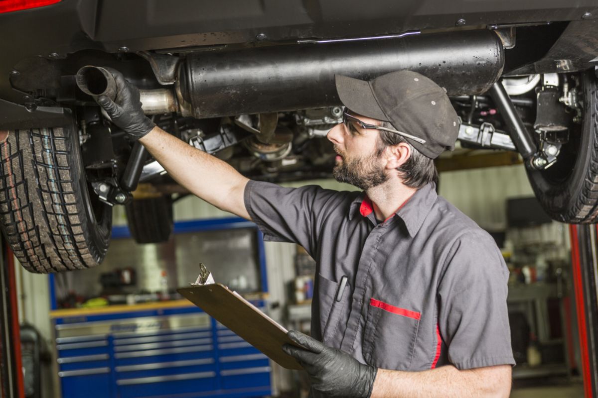 A professional auto mechanic checking the condition of his client's car muffler.