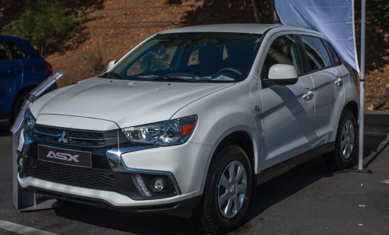 Close up photo of white mitsubishi car parked outside.