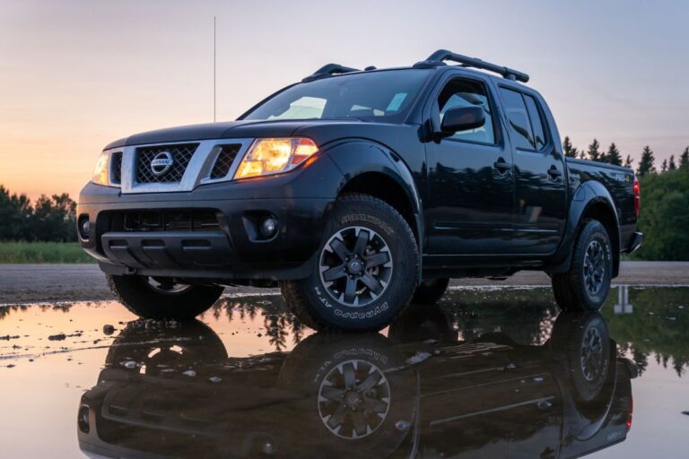 A photo of black nissan frontier at wet surface with reflection in puddle on side of the road.