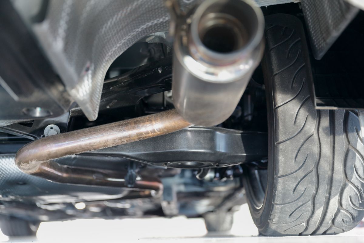 A photo of car's suspension and exhaust pipe with shield for mufflers.