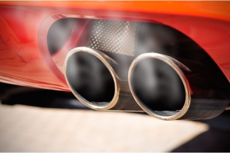 A zoom in photo of a smoking double exhaust pipe of a sports car ready to go.