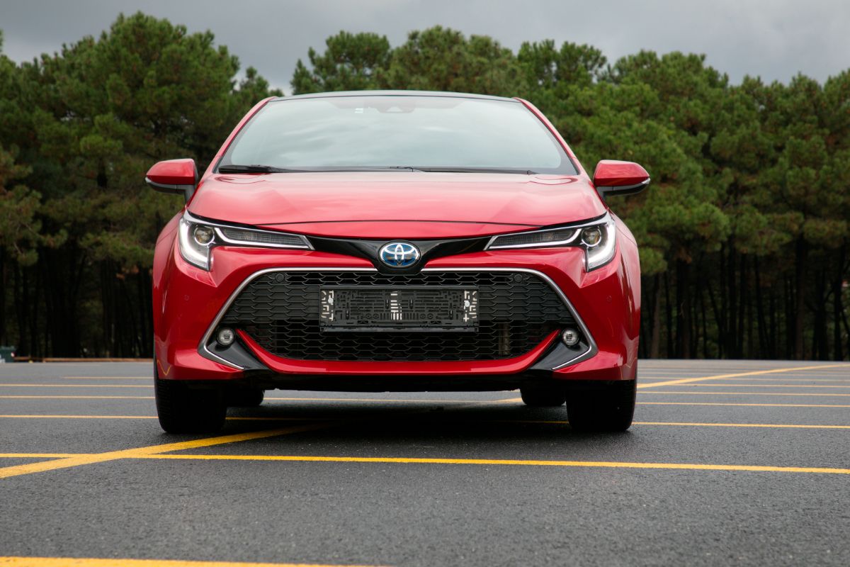 Front view look of red toyota corolla hatchback in the parking lot with trees background.