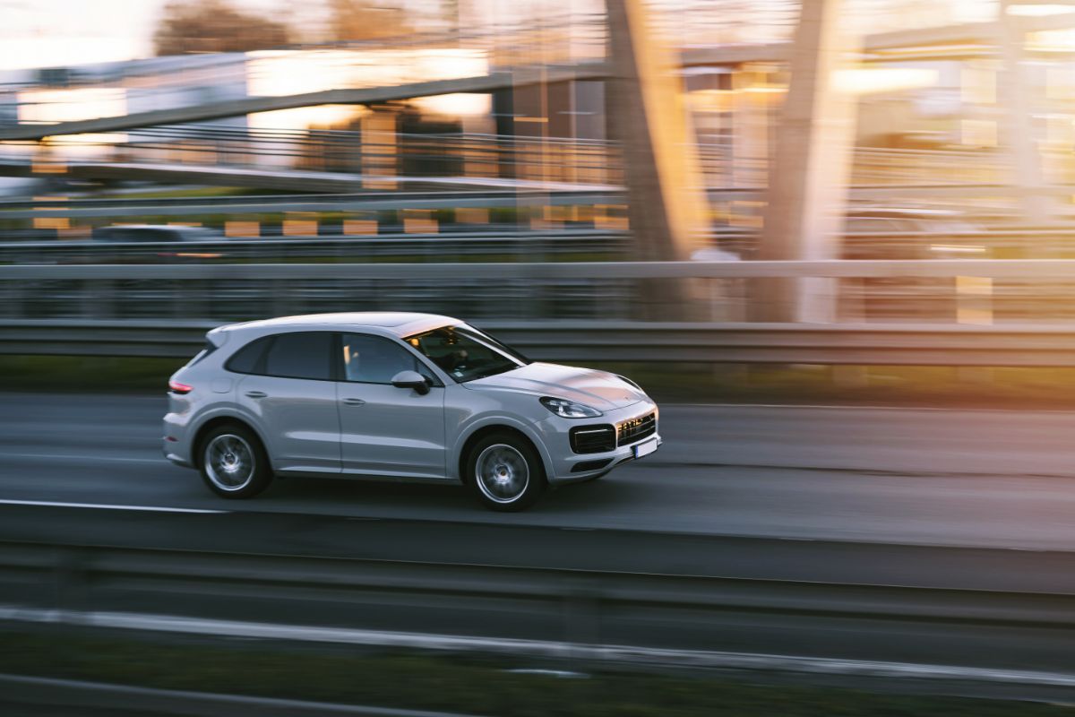 In the late afternoon sun, a brand-new Porsche Cayenne S sports car travels at a fast rate of speed on a motorway.