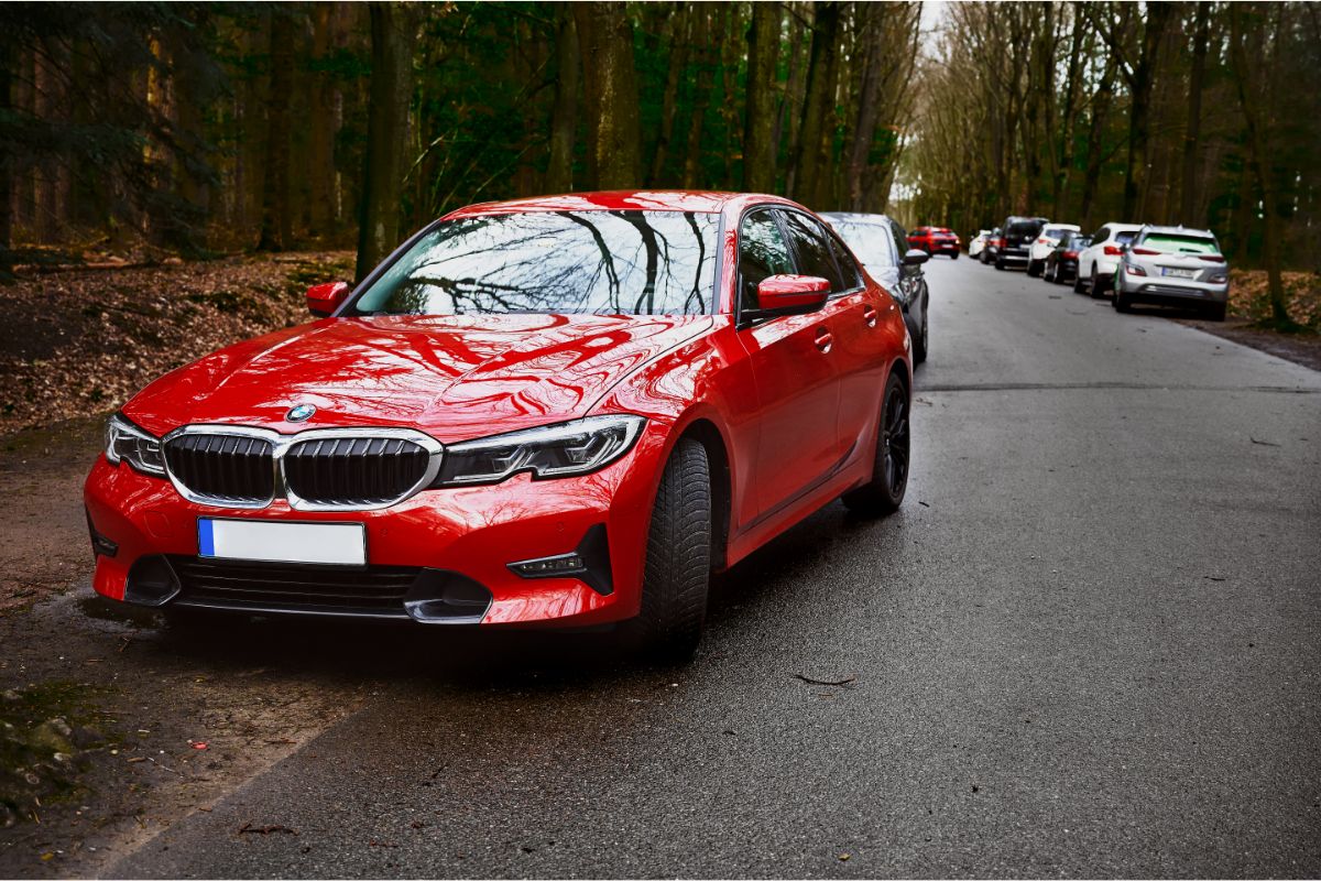 In the woods, a red BMW 3 series is parked on the side of the road.