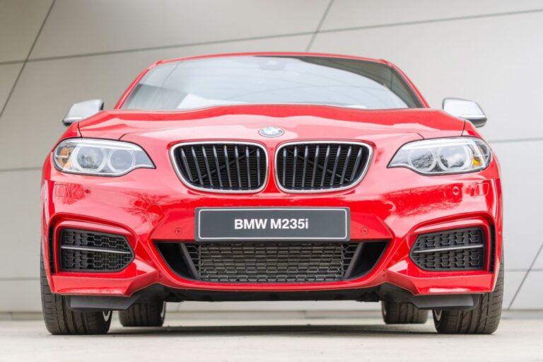 Front view of red BMW M235i on a wide wall background.