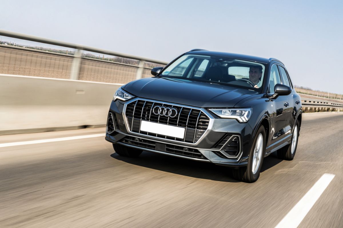 Motion view of a man driving a gleaming black Audi Q3 car on the road.