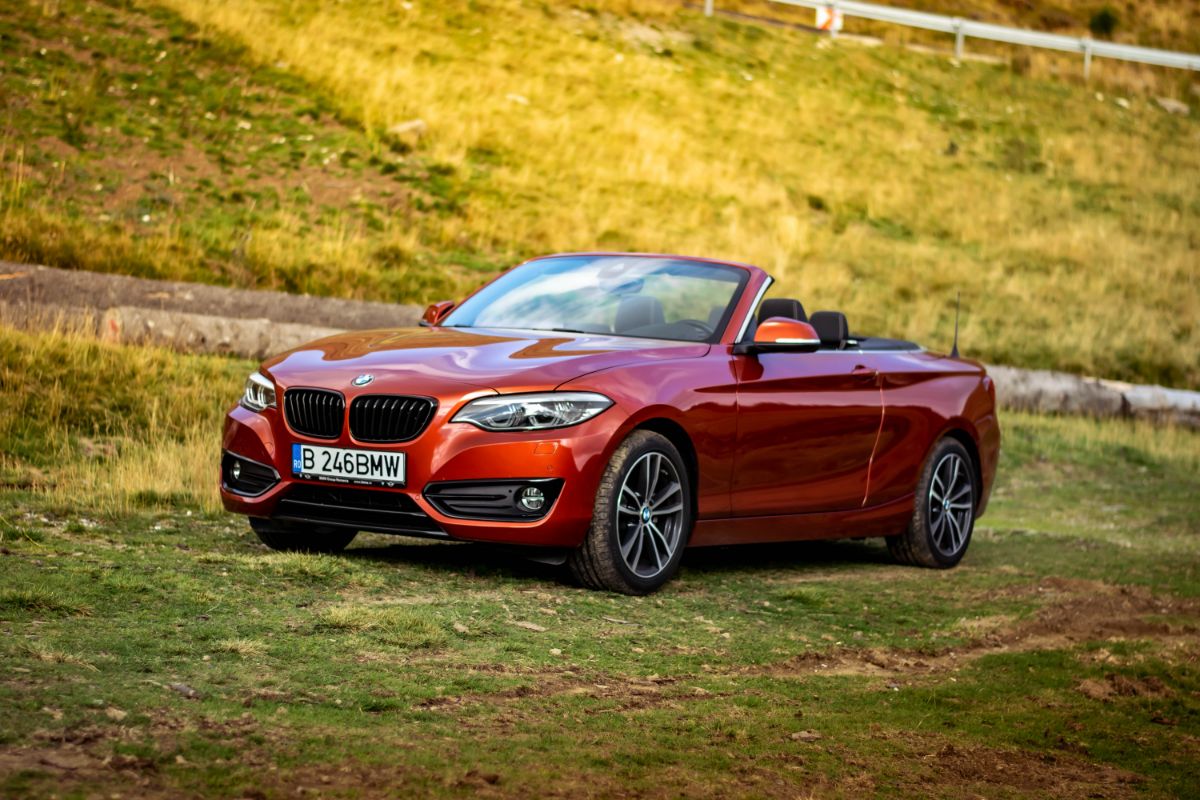 A glossy red BMW 2 Series with an open roof is parked on the field as seen from the front.