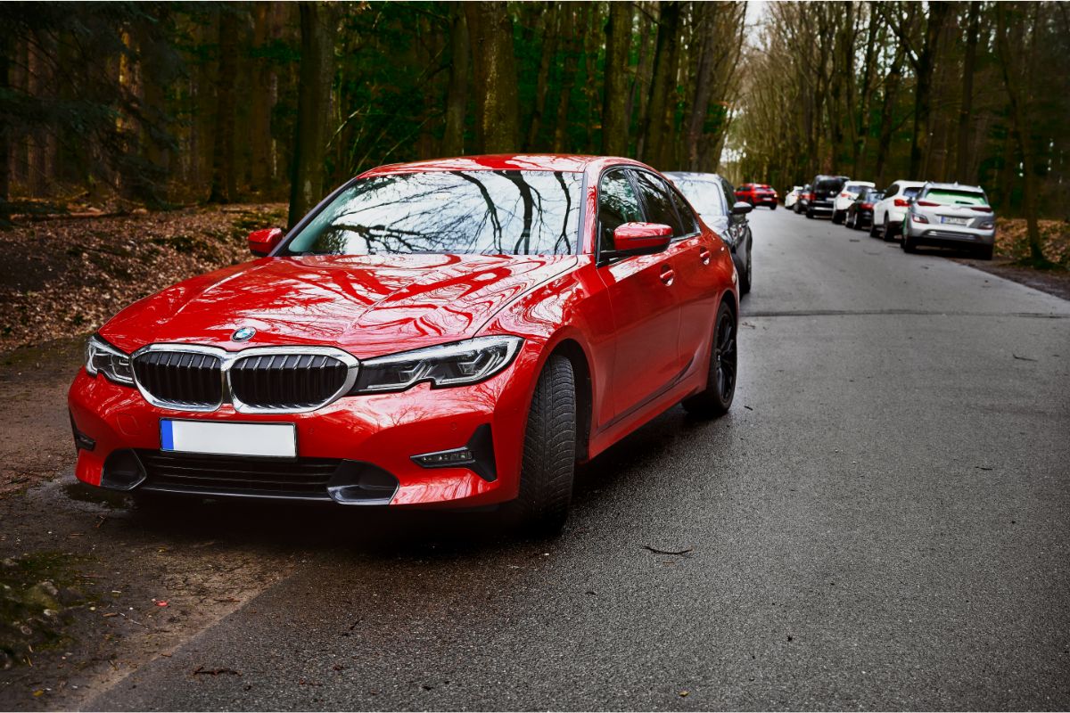 A red BMW 3 Series parks on the side of the road in the woods.