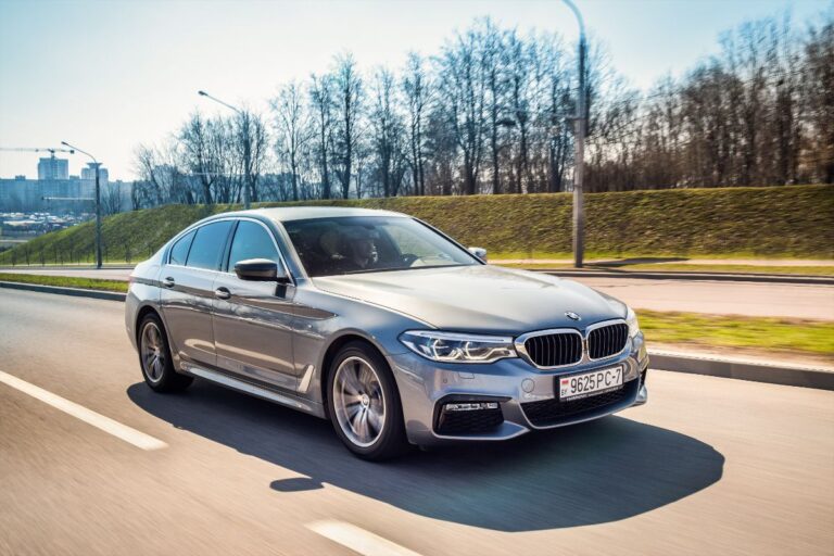 Running silver BMW 5 Series with city and tree background.