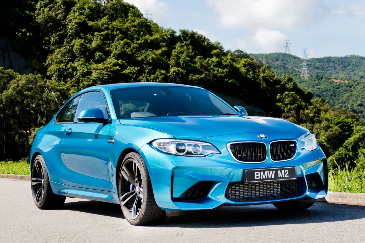 Front side view of a gleaming sky blue colored BMW M2 parked on the mountain road.