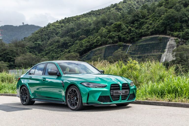 A new BMW M3 car in a green color test driving on the road with mountains background.