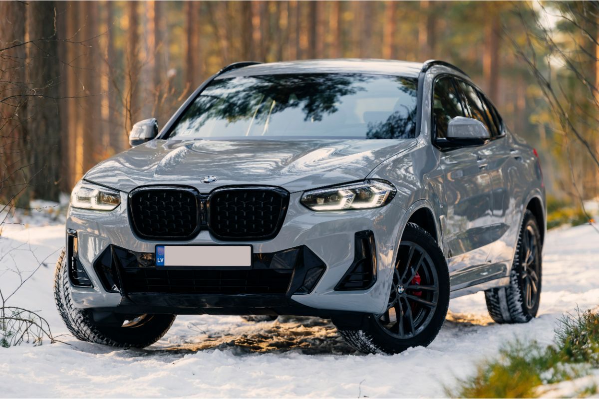 A shiny silver-colored car in the forest during winter.