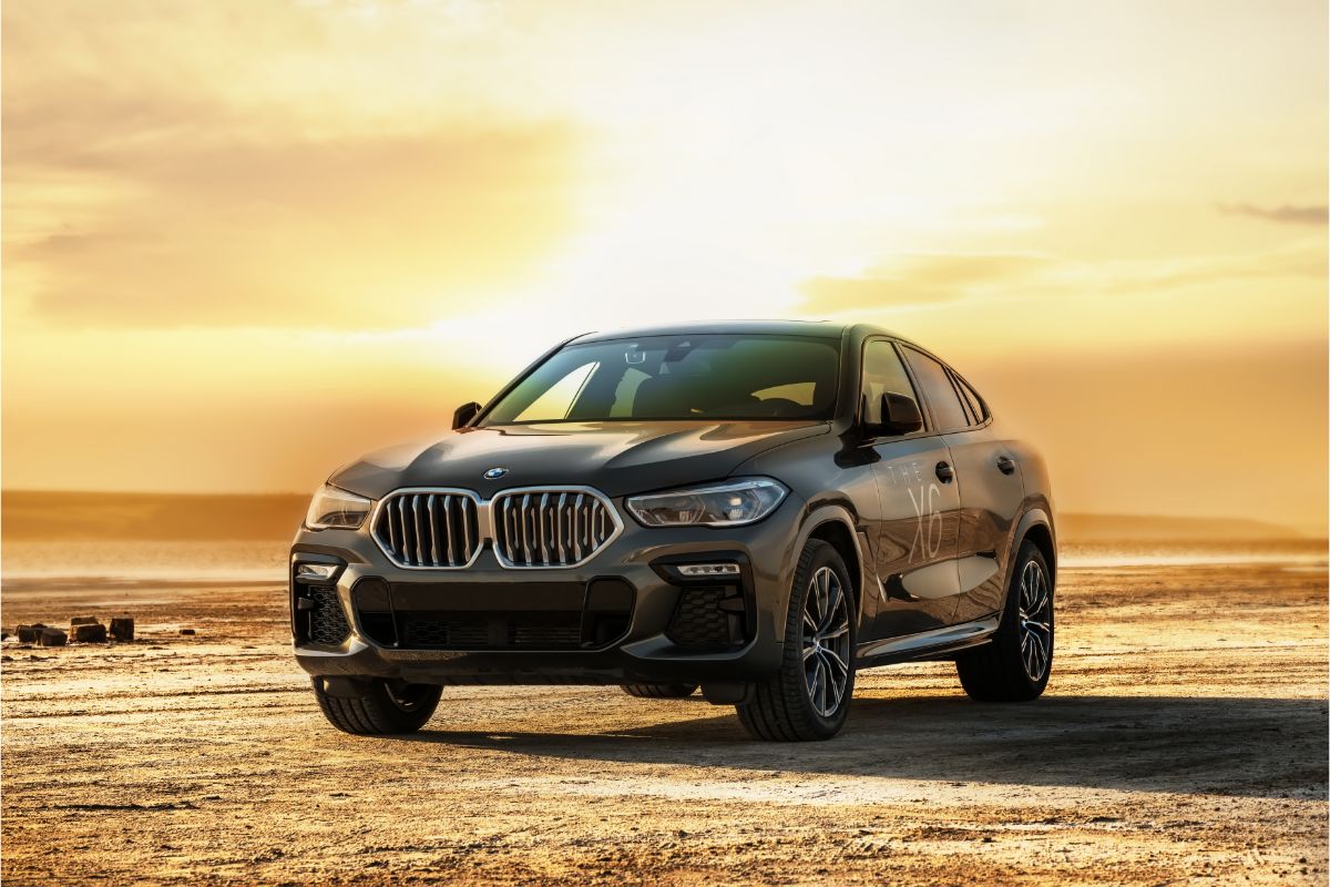 A full view of a black BMW X6 car on a lake at sunset.