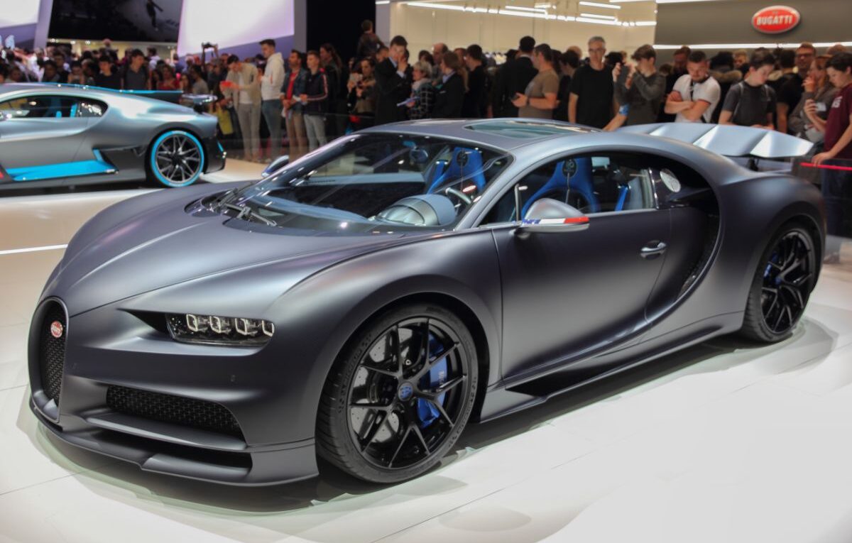 Side view shot of grey Bugatti Chiron displayed at the motor show full of people.