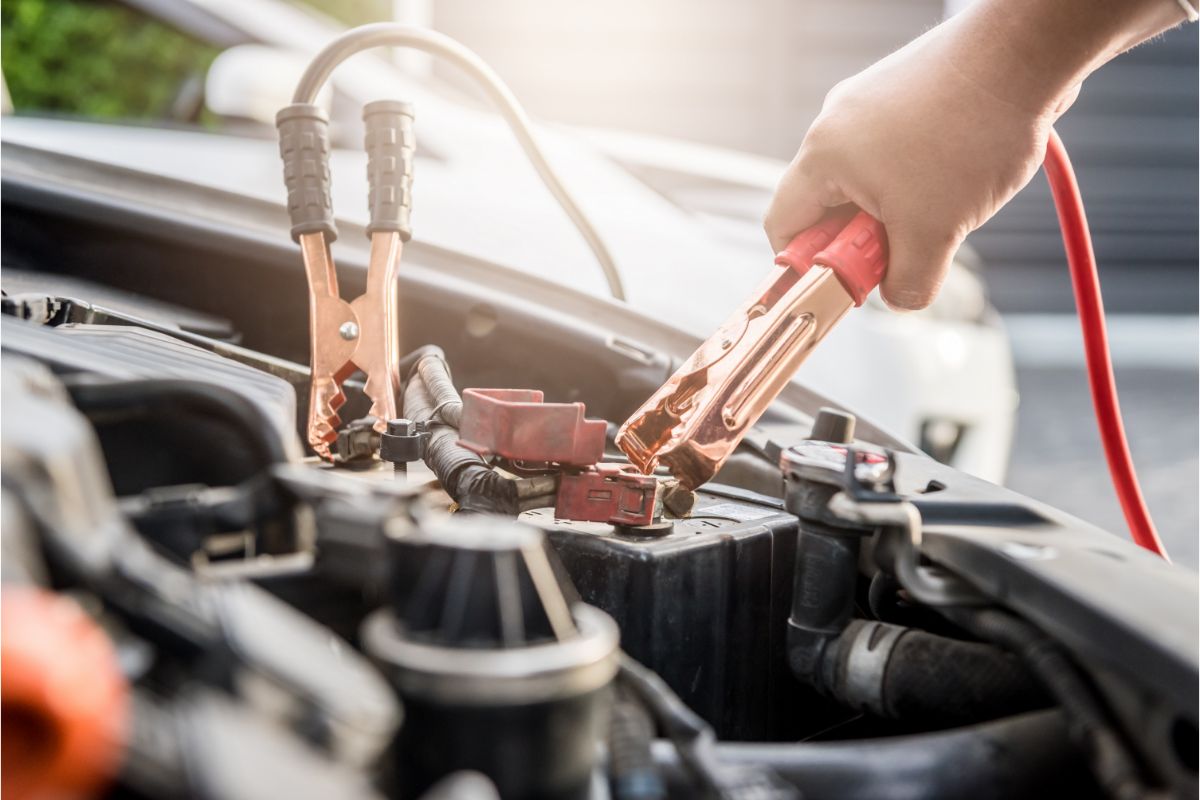 Close-up of a hand using jumper cables to charge an automobile battery with power.