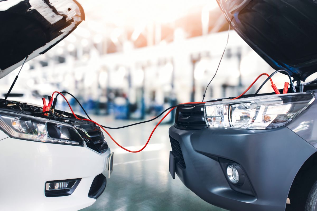 A picture of a sedan automobile in a repair shop jumping the pickup truck's battery cables