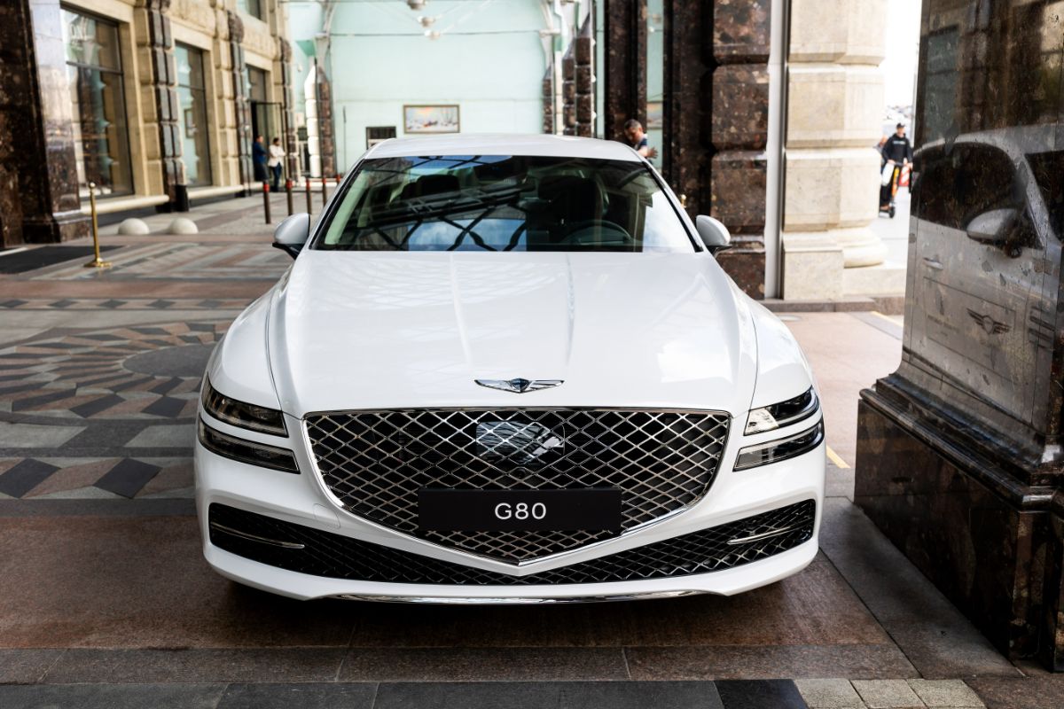 Front view of white Genesis G80 car parked near the hotel.