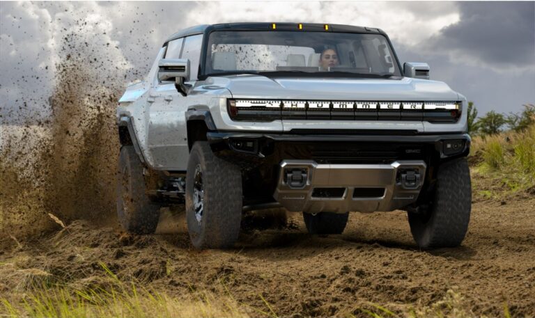 Front view of the all new GMC Hummer EV with a lady driver driving by in the wet sand terrain.