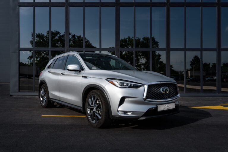 Silver Infiniti QX50 on parking lot in front of glass wall.