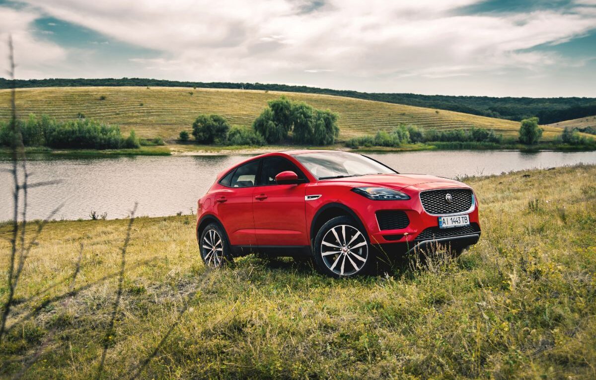 A red Jaguar E-Pace car parked on the field with river behind it.