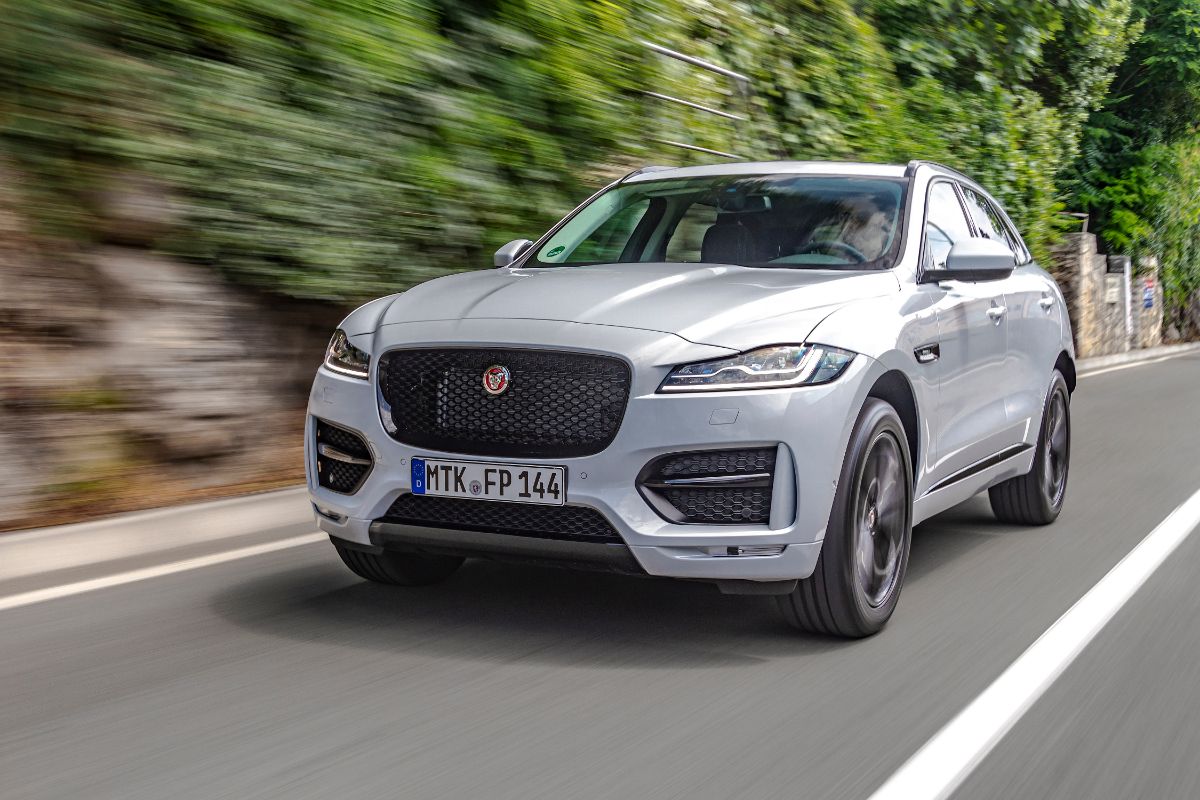 Motion view of a man is driving new Jaguar F-Pace fast on a country road.