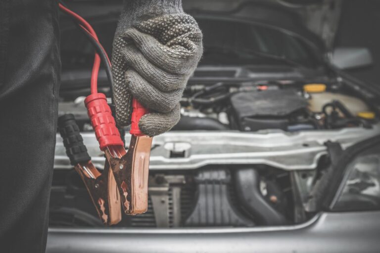 A battery that has been discharged is being charged in the garage by a car mechanic wearing gloves.